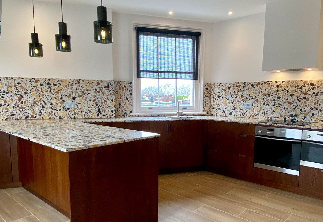 Kitchen interior design in Kensington with terrazzo countertops and splashback complemented by smoky glass pendant lamps.