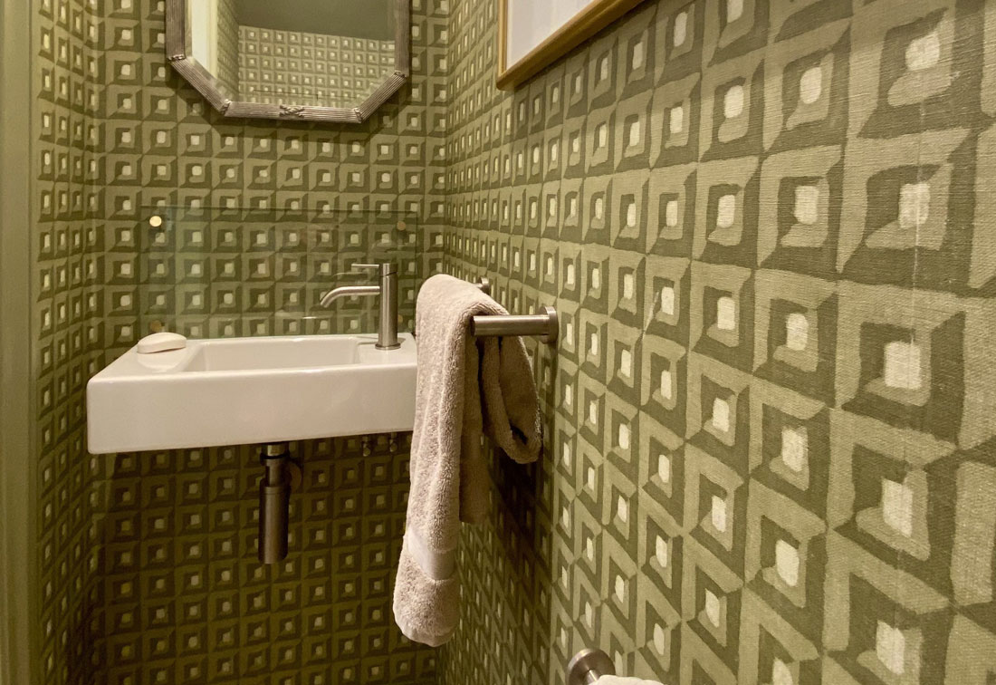 Close up of the textured green wallpaper, white ceramic sink and vintage mirror in this Wandsworth family home.