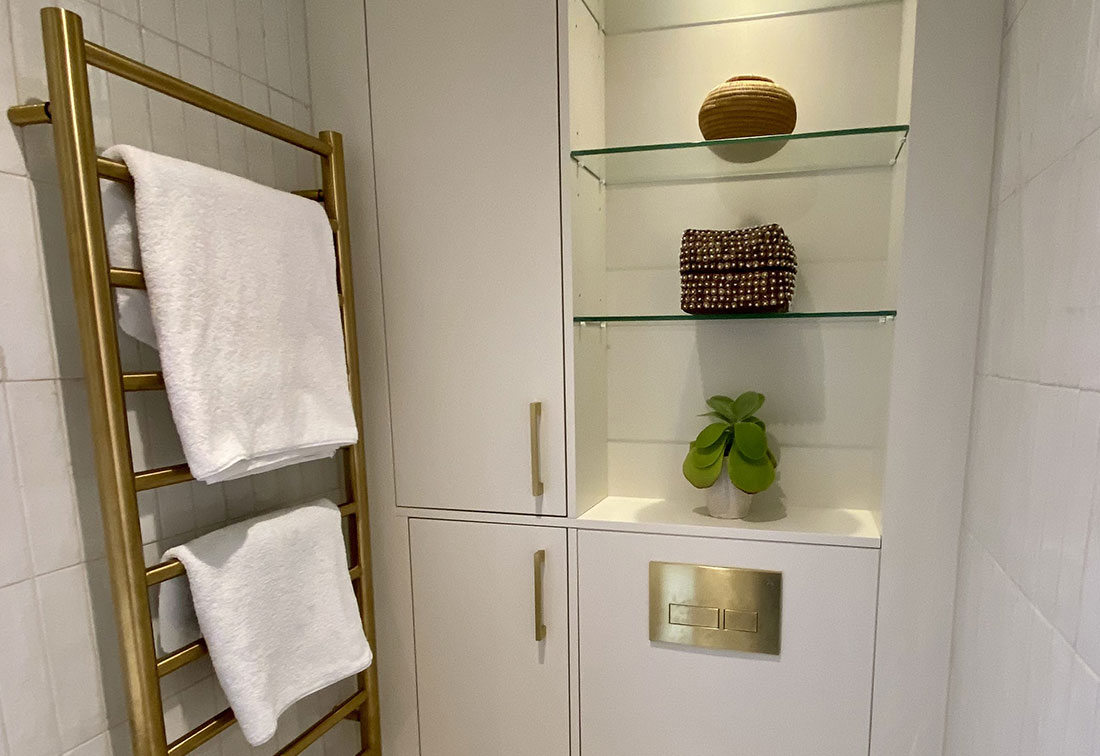 Bathroom interior design in SW6 in neutral tones with a bronze towel rail and glass shelves for ornaments.