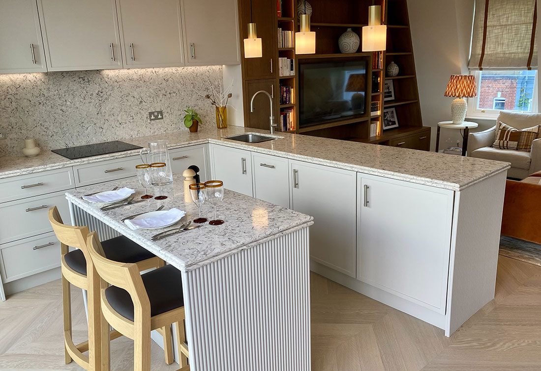 Neutral kitchen design in Fulham with marbled tops, a kitchen island with wooden high stools and glass pendant lamps.